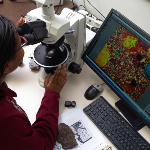 Woman looks at cells through a microscope.